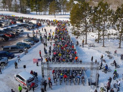 Large group of bike riders waiting in line at the beginning of a race on a snowy day outside.