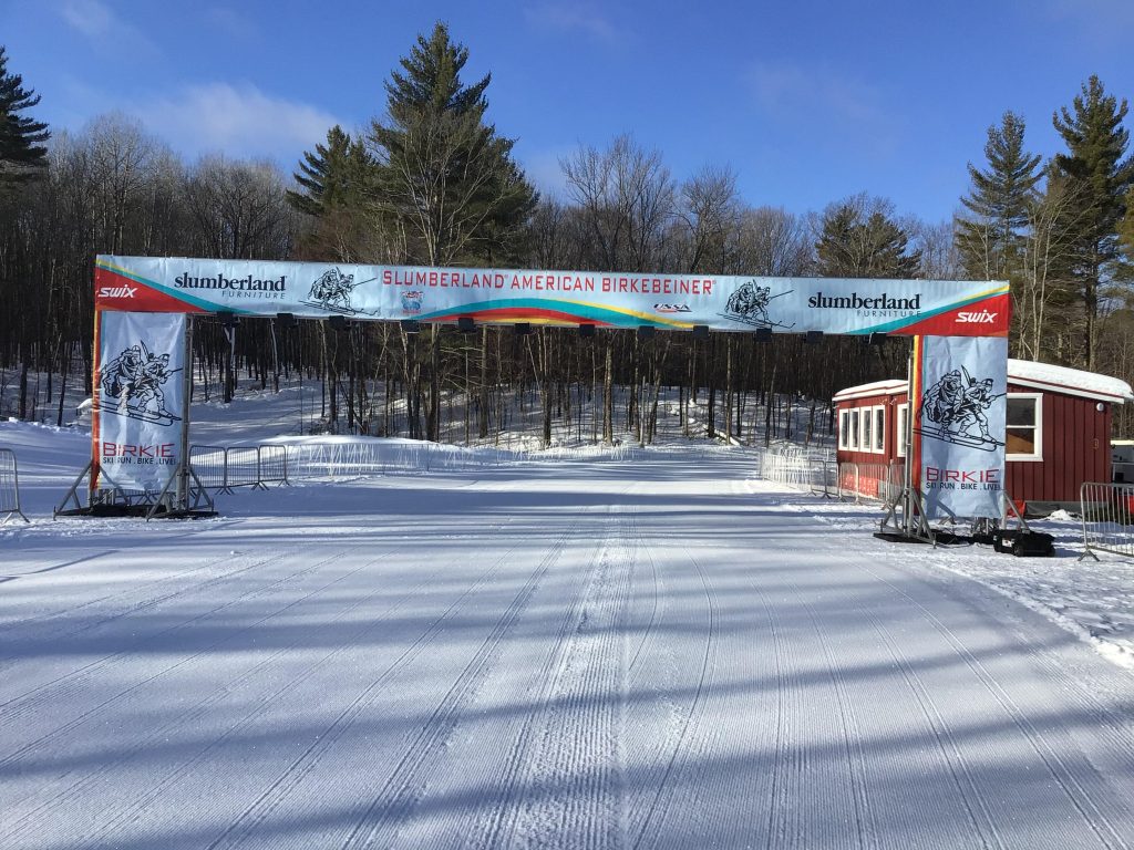 Large truss structure set up outside on a snow covered road with trees in the background.