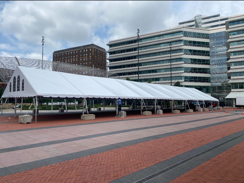 Frame tent with gable end set up outside in front of large office building.
