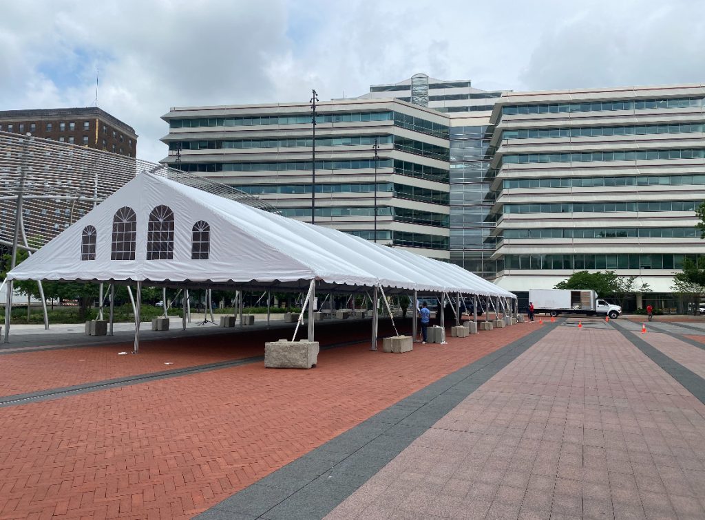 Frame tent with gable end set up outside in front of large office building.
