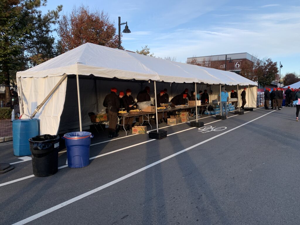 Several people standing under a 10' x 60' frame tent set up outside.