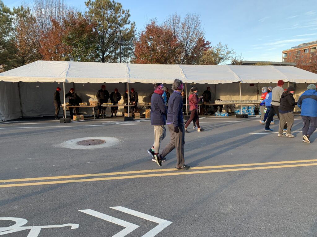 Several people standing under a 10' x 60' frame tent set up outside.