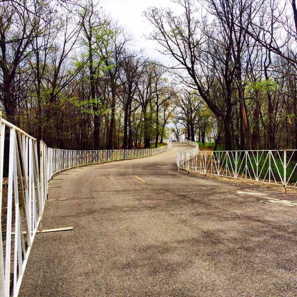 Winding street with trees on each side of a white barricades.