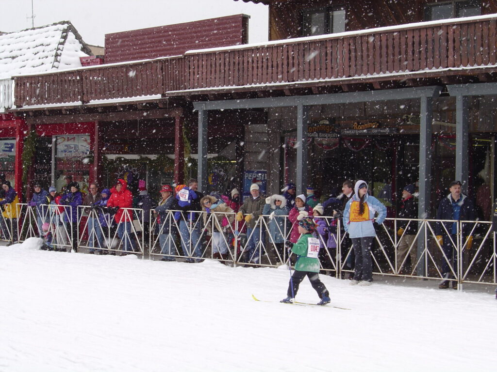 Spectators standing outside beside French barricades while it snows.