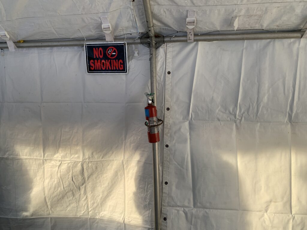 No Smoking sign and fire extinguisher hanging on the inside of a white tent.