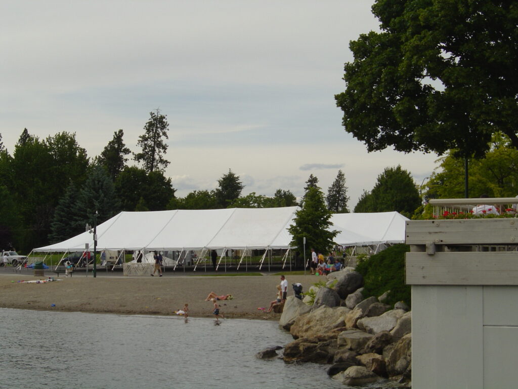 Large white tent set up outside with lake in the foreground.